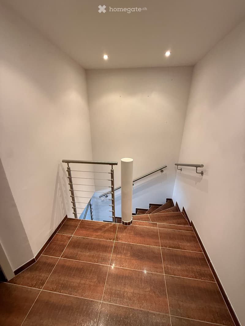 Modern staircase with brown tiled steps, white walls, and stainless steel railings.