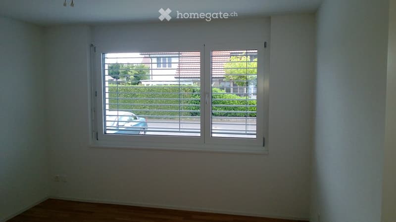 Empty room with light-colored walls and wooden flooring, featuring two large windows with white frames and blinds.