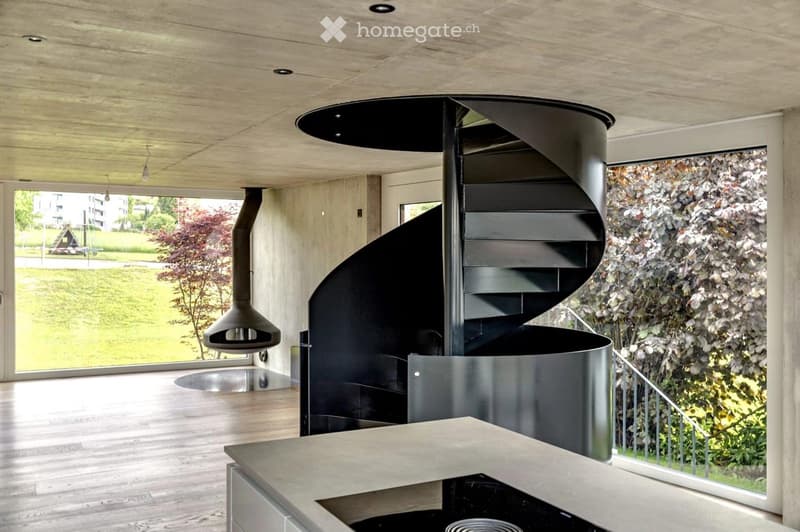Modern hallway with a sleek black spiral staircase, wooden ceiling, and large windows overlooking a green landscape.