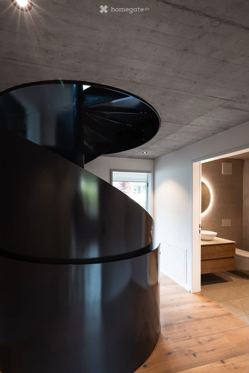 Modern bathroom with wooden flooring, a sleek black spiral staircase, and a built-in sink and toilet.