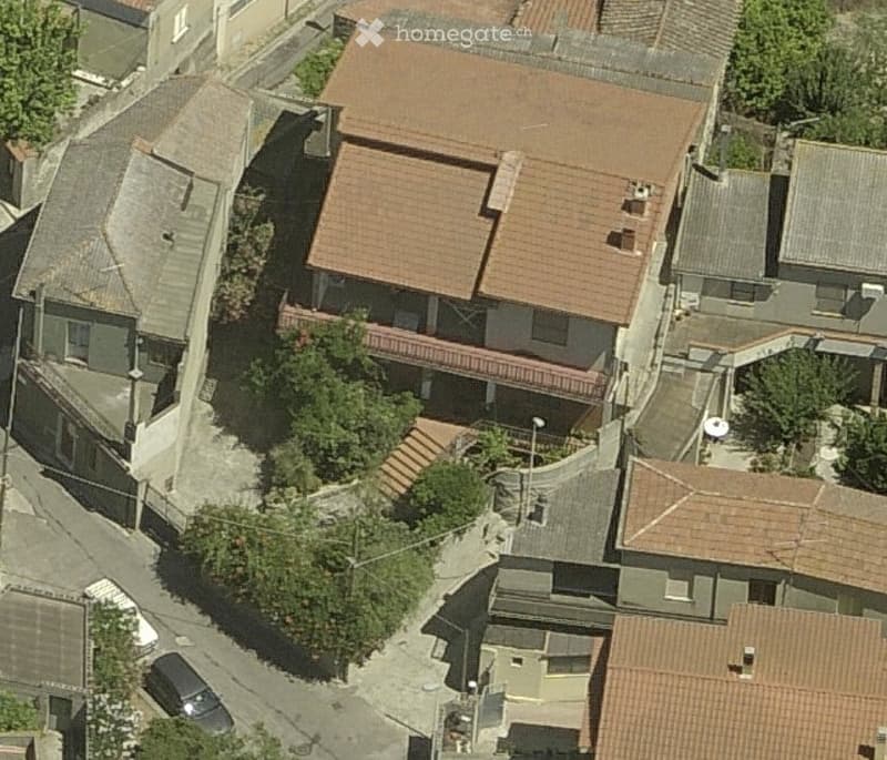 Aerial view of a multi-story residential building with a red-tiled roof, surrounded by neighboring structures and greenery.