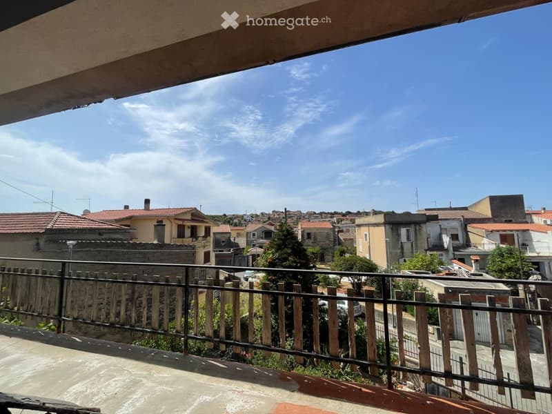 Balcony overlooking a residential area with multiple houses, trees, and a clear blue sky.