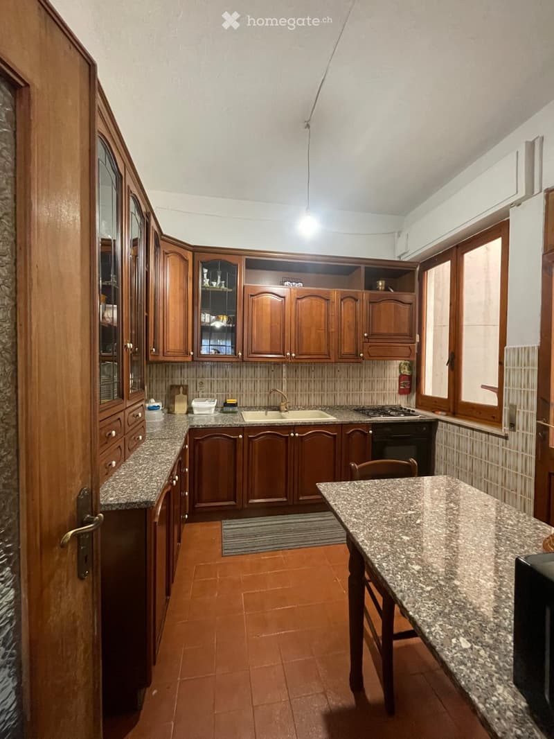 A well-furnished kitchen with wooden cabinets, granite countertops, a sink, stove, and a small dining area with a table and chair.