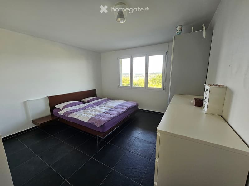 Bedroom with a double bed, nightstand, dresser, and mirror. The room features dark tiled flooring and large windows with a scenic view.