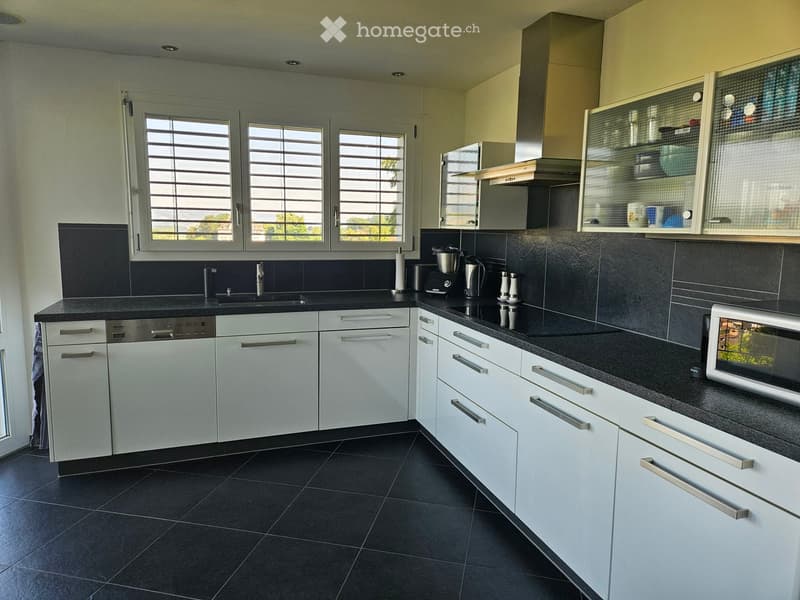Modern kitchen with white cabinets, black countertops, and stainless steel appliances. Features include a sink, dishwasher, microwave, coffee maker, and various kitchen items on the counter.