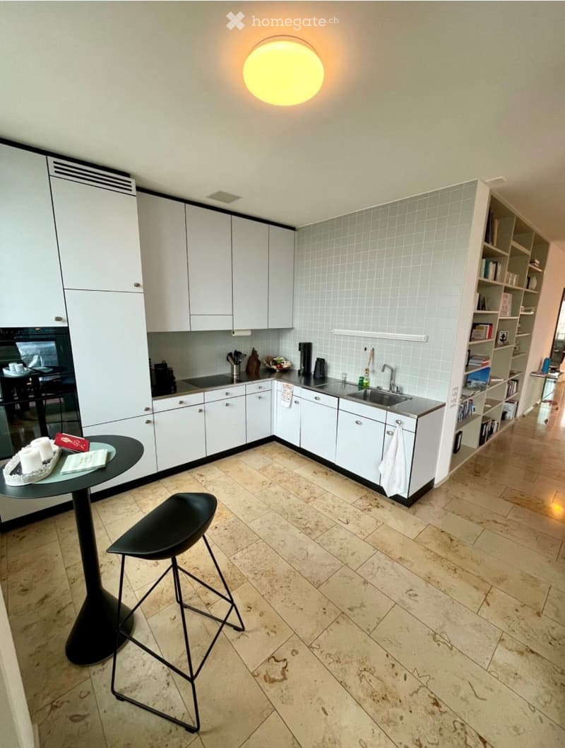 Modern kitchen with white cabinets, a black stool, a round table, and a sink with a faucet.