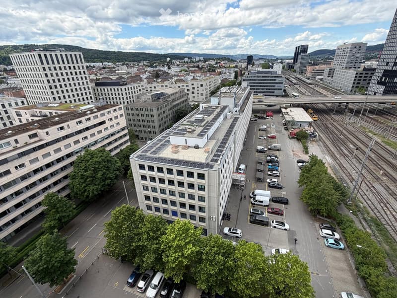 Aerial view of a modern urban area with multiple buildings, parking lots, and a train track running alongside.