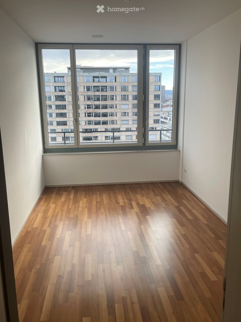 Empty room with wooden flooring and large windows offering a cityscape view.
