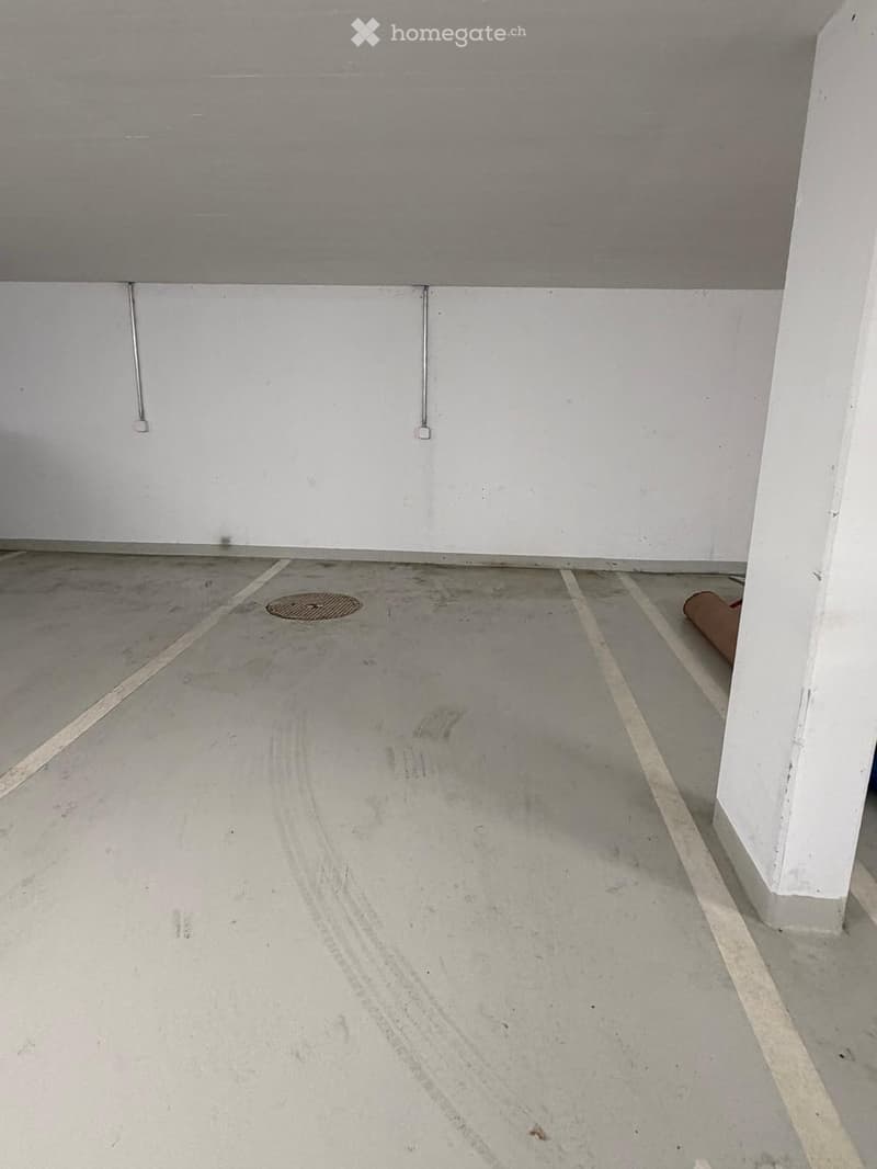 Empty room with concrete floor and white walls, featuring a drain in the center and electrical outlets on the walls.