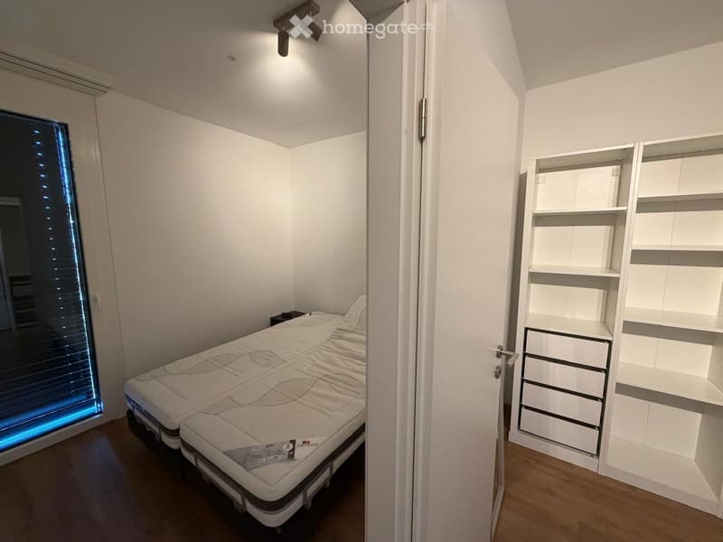 Modern bedroom with a large bed, white wardrobe with shelves and drawers, and a window with blinds.