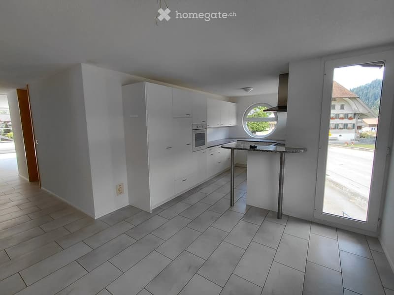 Modern kitchen with white cabinetry, stainless steel appliances, and a central island. Features a large window and a round porthole window above the sink.