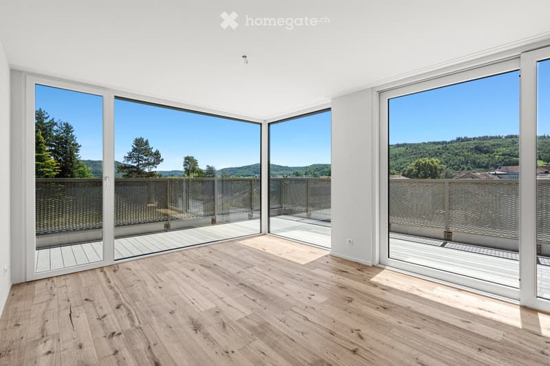 Bright, unfurnished room with large sliding glass doors leading to a balcony, wooden flooring, and a scenic view of greenery and hills.