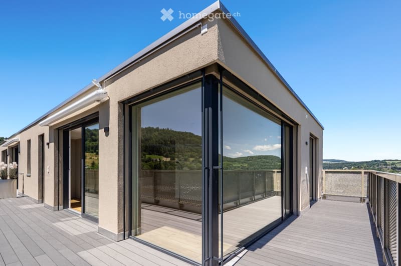 Modern balcony with large glass doors, wooden decking, and scenic mountain view.
