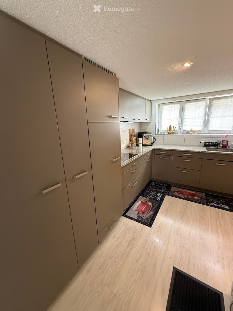 Modern kitchen with light-colored cabinets, stainless steel appliances, and a light wooden floor. The kitchen features a coffee maker, sink, and various small appliances on the counter.