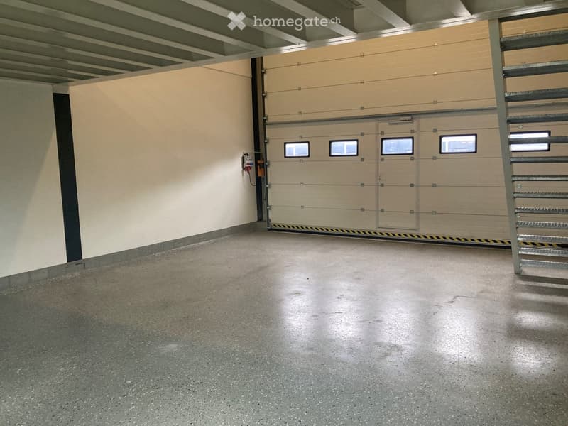 Empty underground garage with concrete floor, beige walls, and multiple garage doors with small windows.