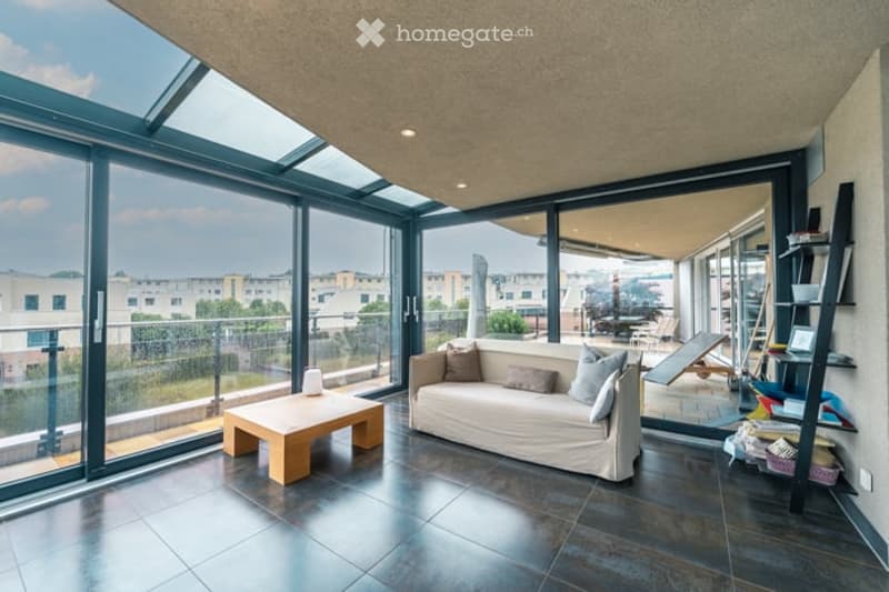 Modern living room with large glass windows and a balcony, featuring a sofa, coffee table, and shelves.