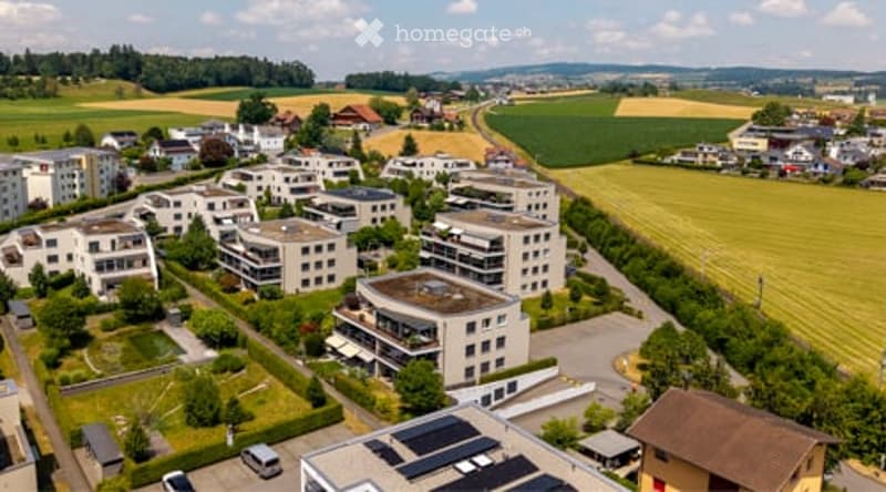 Aerial view of a residential area with multiple apartment buildings, surrounded by green fields and scattered trees.