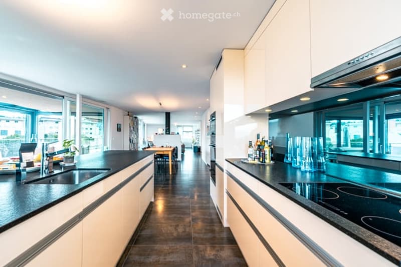 Modern kitchen with white cabinets, black countertops, and stainless steel appliances. Features a central island with a sink and stove, a dining area with a table and chairs, and large windows offering a view.