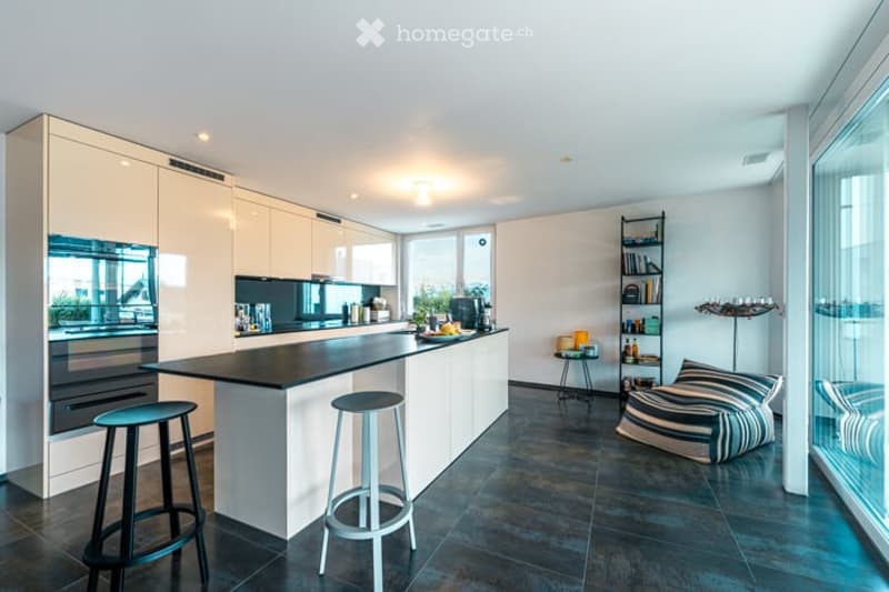 Modern kitchen with white cabinets, black island, and stainless steel appliances. Features include a coffee maker, microwave, and a small seating area with a bean bag chair and a small table.