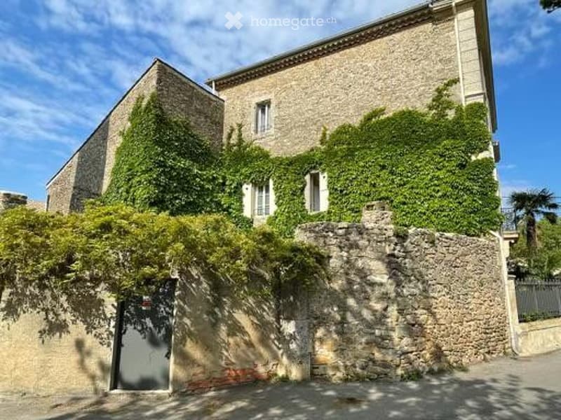 A two-story stone building with ivy-covered walls, multiple windows, and a gated entrance.