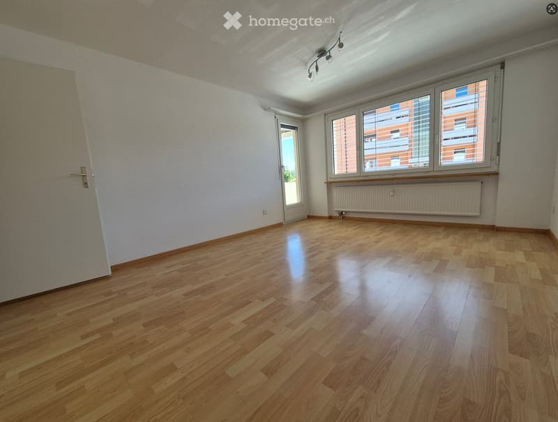 Empty room with wooden flooring, white walls, large windows, and a radiator. No furniture or equipment present.