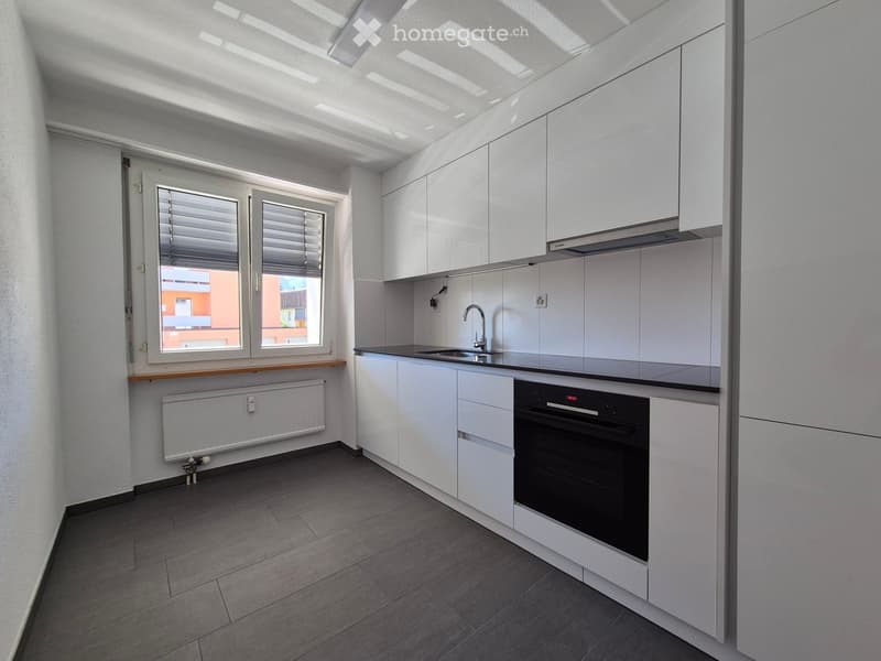 Modern kitchen with white cabinets, a black oven, a sink with a faucet, and a window with blinds.