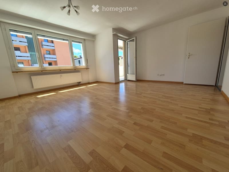Empty room with wooden flooring, large windows, and a radiator. No furniture or equipment present.