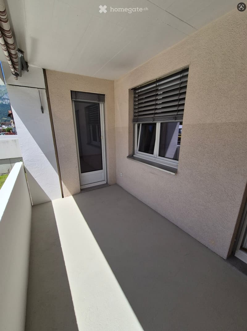 Balcony with a door leading inside, window with blinds, and a view of the surrounding area.