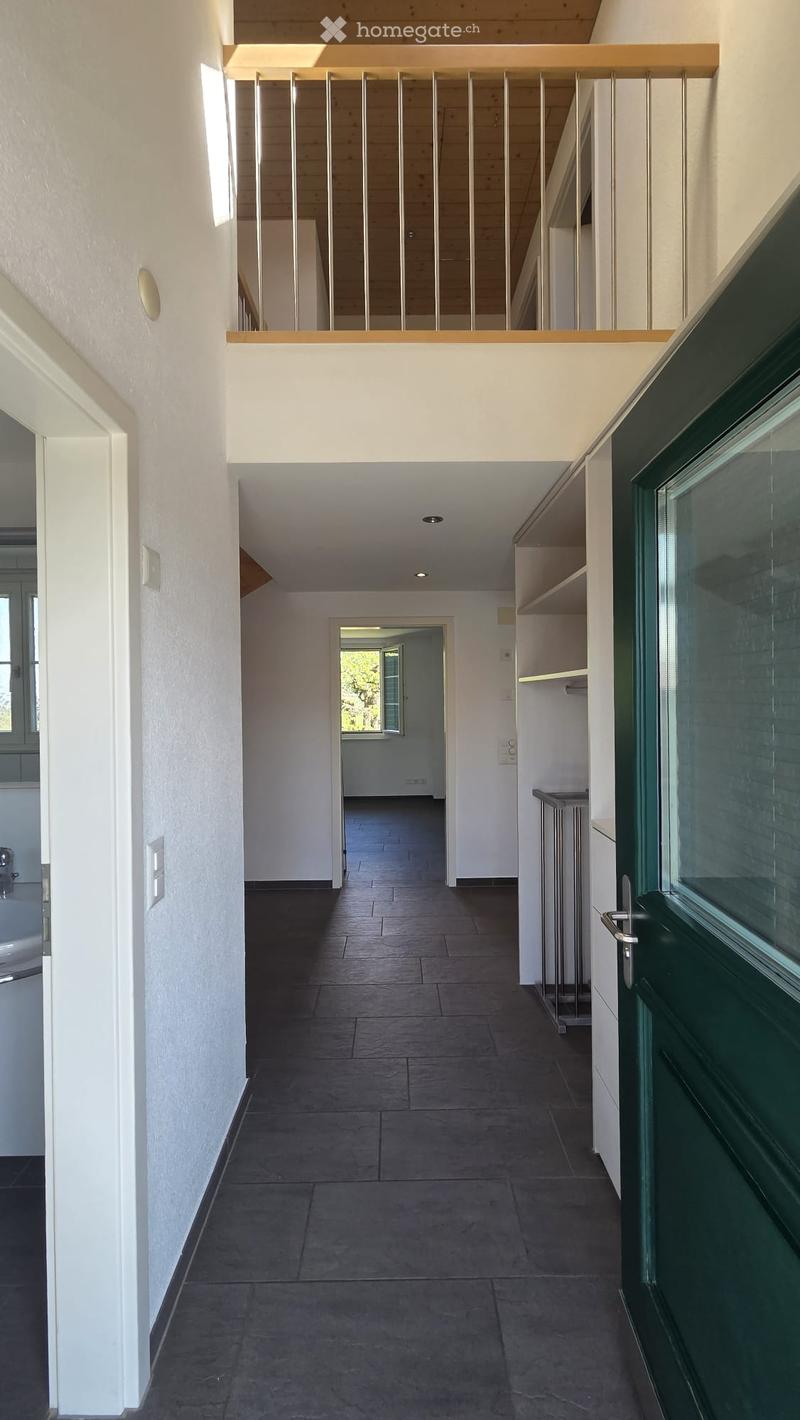 Modern hallway with dark tiled floor, white walls, and a staircase leading to an upper level. Features include built-in shelving, a green door, and recessed lighting.