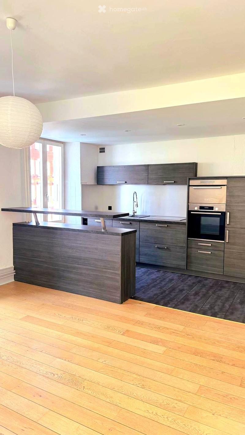Modern kitchen with wooden flooring, dark grey cabinets, stainless steel oven, and a central island counter.