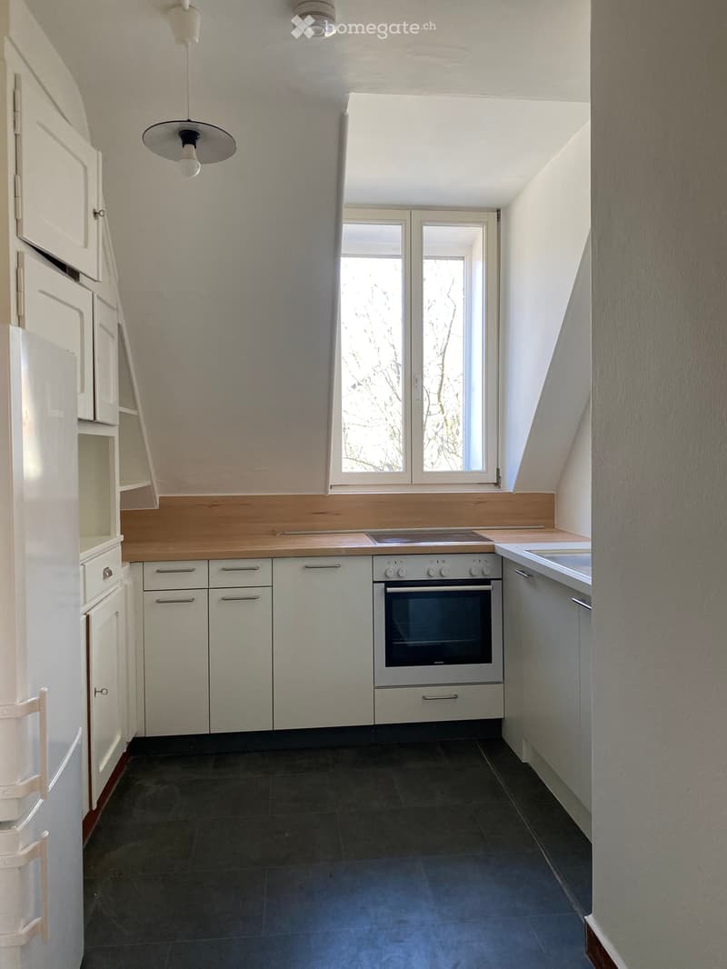 Modern kitchen with white cabinets, stainless steel oven, dark tiled floor, and a window with wooden trim.