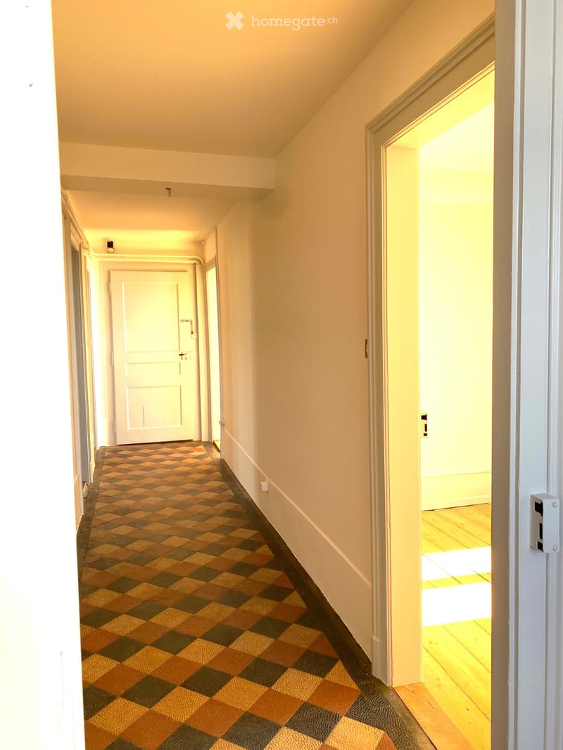 A narrow hallway with a checkered carpet, white walls, and several doors leading to other rooms.