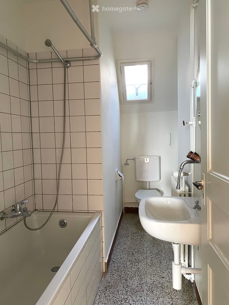 Bathroom with a bathtub, toilet, and sink. The bathtub has a handheld shower attachment, and the sink is mounted on the wall. There is a small window above the toilet.
