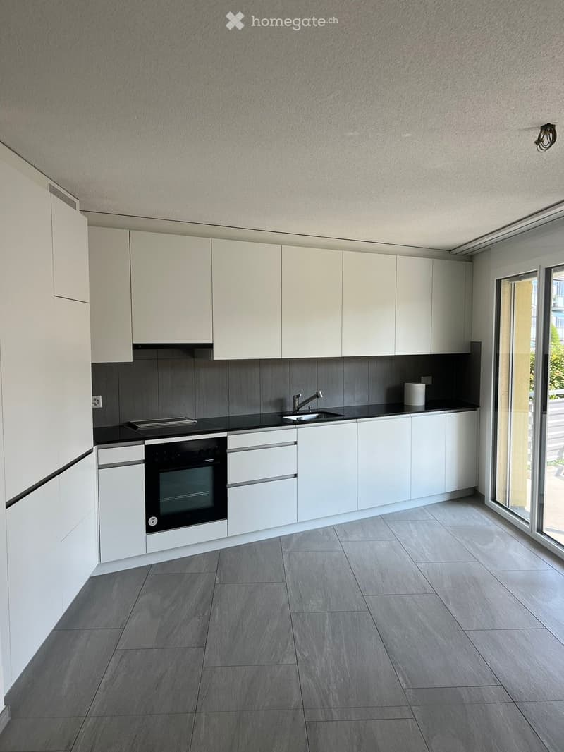 Modern kitchen with white cabinets, grey tiled backsplash, and grey tiled floor. Features an oven, sink, and faucet.