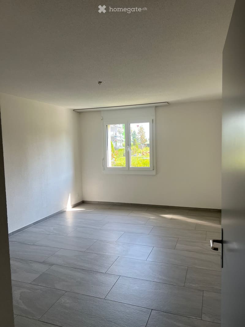 Empty room with grey tiled floor, white walls, and a large window with blinds. No furniture or equipment present.