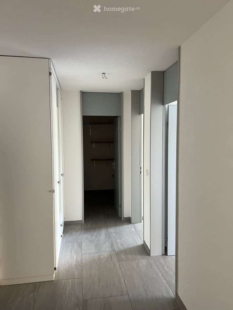 Empty hallway with grey tiled floor, white walls, and several closed doors leading to other rooms.
