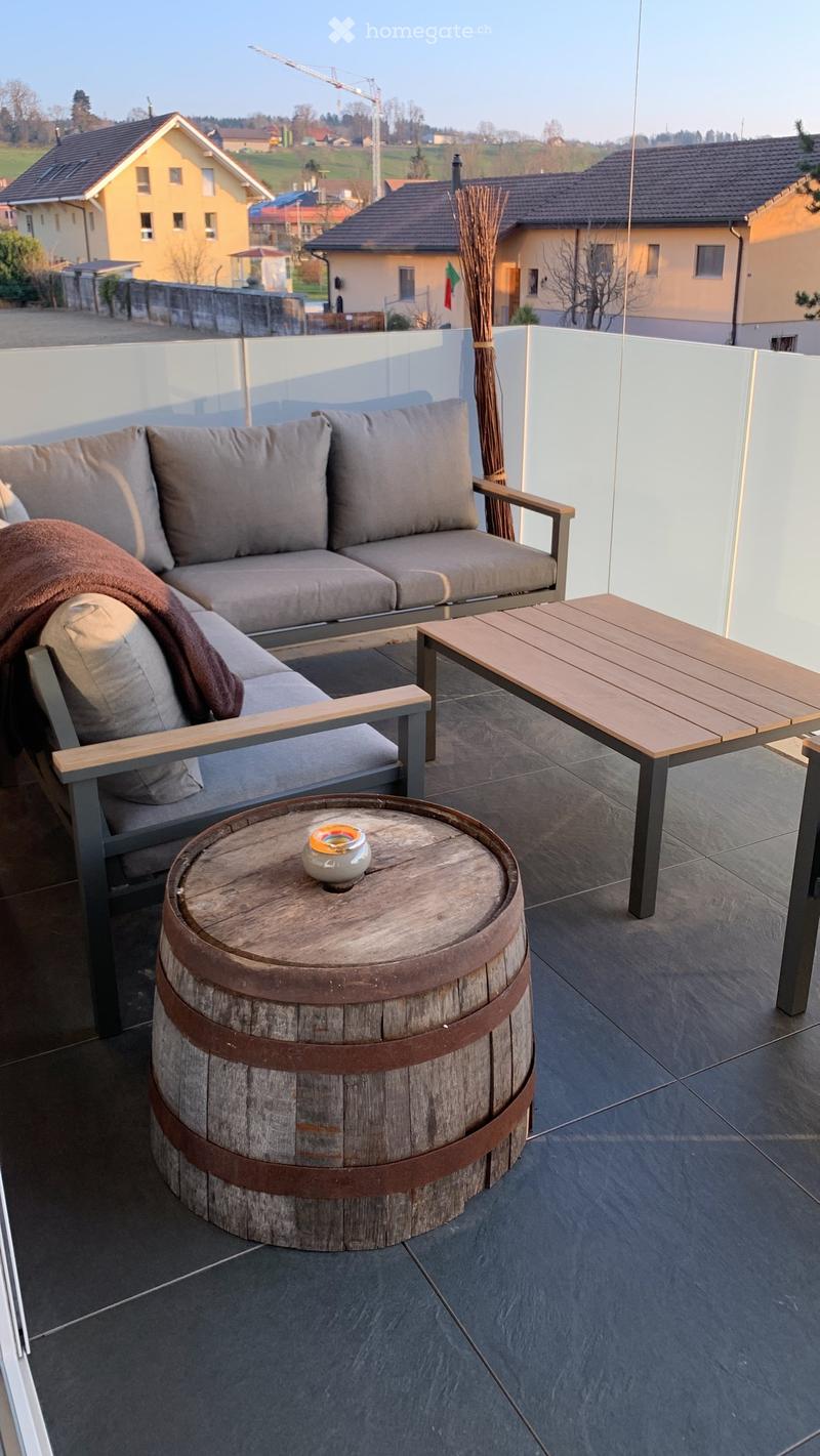 A balcony with furniture and a barrel, with a view of the village