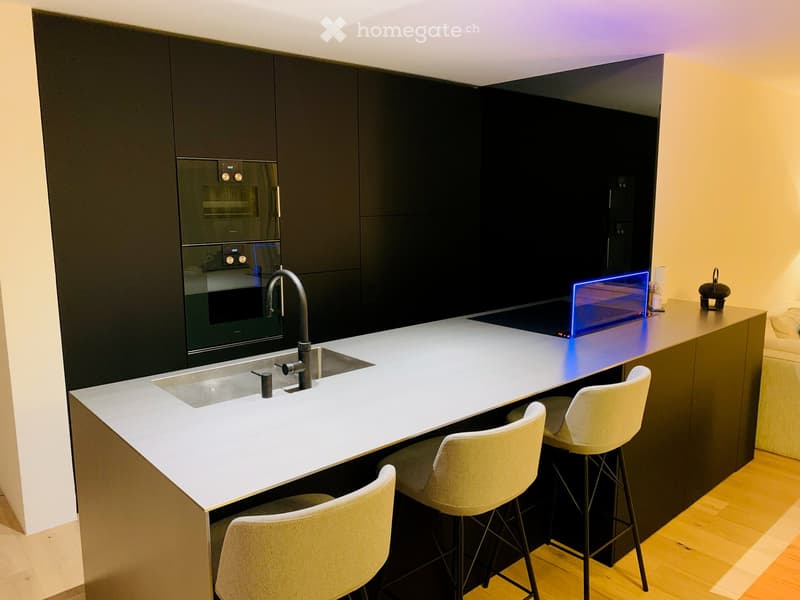 modern kitchen with dark cabinets, a white island with a sink and faucet, black bar stools, and a stove