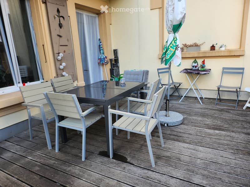 Balcony with wooden decking, glass table, several chairs, and an umbrella.