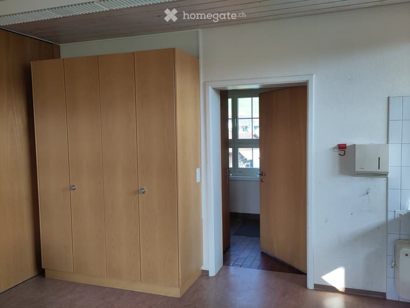 Empty room with wooden cabinet, open doorway leading to another room, tiled walls, and a visible light switch.
