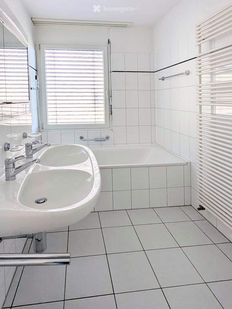 Modern bathroom with white tiles, a sink with a modern faucet, a bathtub, and a radiator on the wall.