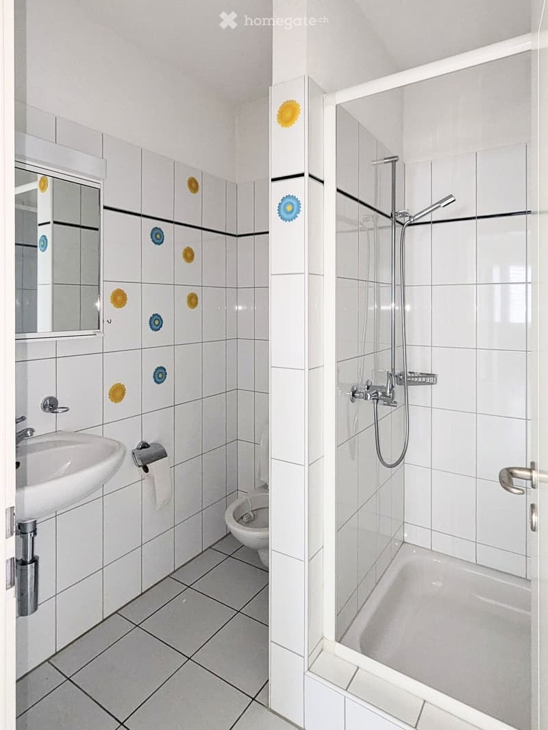 Bathroom with white tiles, a sink, toilet, bathtub, and shower. Features a glass shower enclosure and a mirror with decorative tiles.