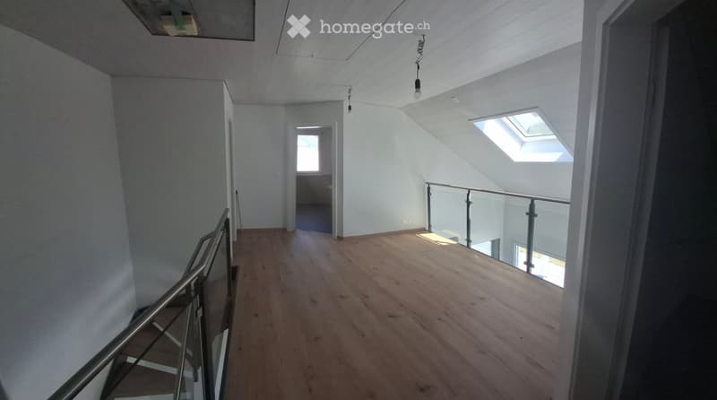 Empty hallway with wooden flooring, white walls, and a modern metal railing leading to a room with a skylight window.