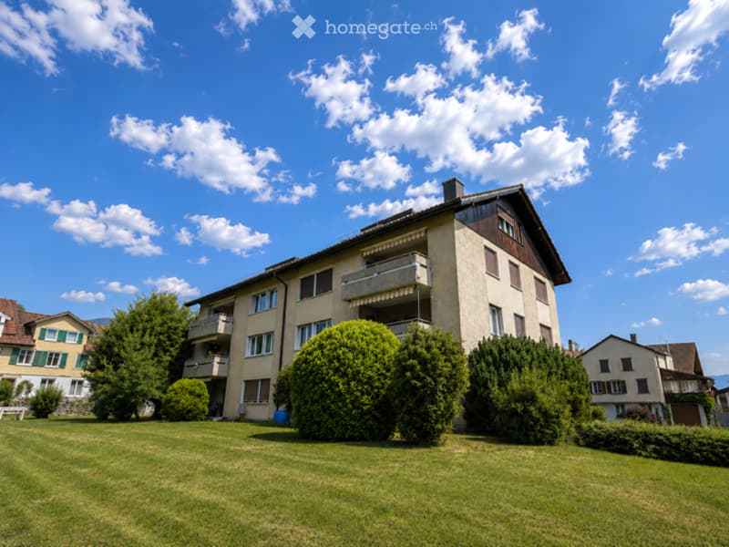 A multi-story residential building with balconies, surrounded by well-maintained green lawns and trees.
