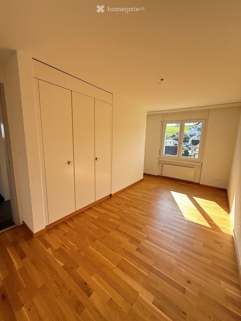 Empty room with light wooden flooring, white walls, built-in closet, and a window with a view of the outside.
