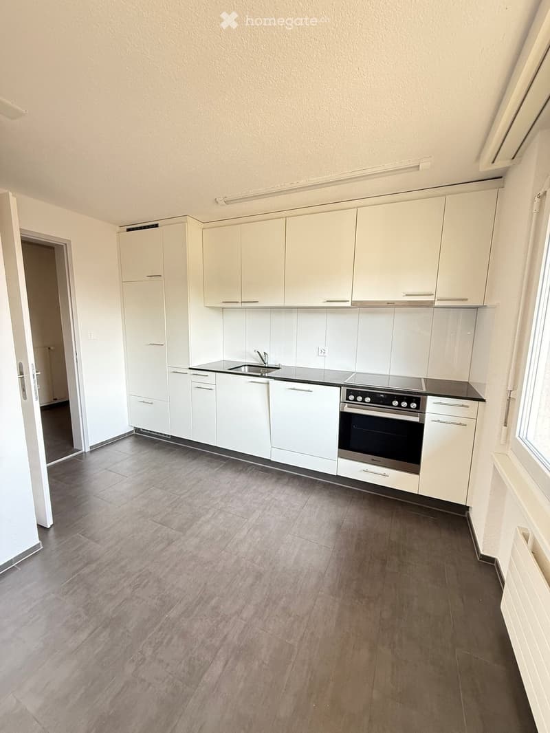 Modern kitchen with white cabinets, a sink, and an oven, featuring a tiled backsplash and wooden flooring.