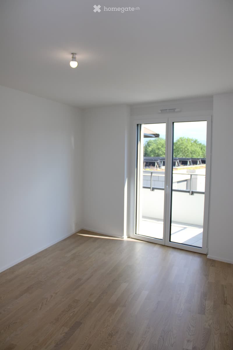 Empty room with wooden flooring, white walls, and a large sliding glass door leading to a balcony.
