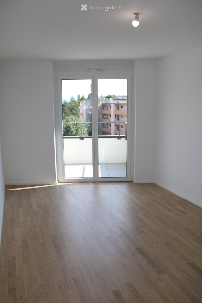 Empty room with light wooden flooring, white walls, and a large glass door leading to a balcony.
