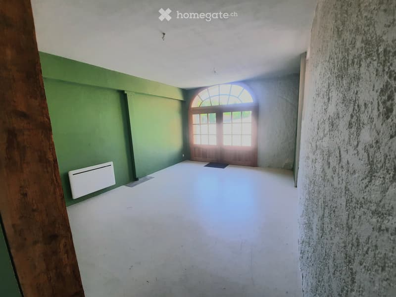 Empty room with white flooring, green and white walls, a wooden door with a glass transom window, and a white radiator on the left wall.