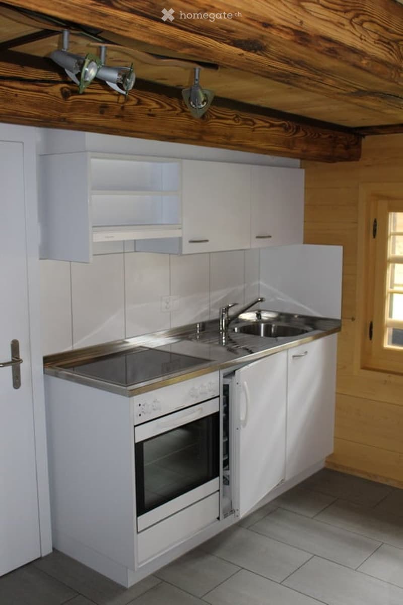 Modern kitchen with white cabinets, stainless steel sink, and built-in oven. Exposed wooden ceiling beams and warm lighting.